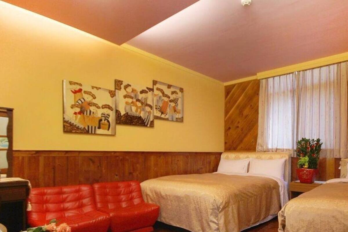 A room with two beds, a red sofa, wooden paneling, and artwork on the wall.