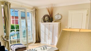 Un salon avec un canapé blanc, une table basse, une lampe et une vue sur l’extérieur, visible à travers une porte vitrée.