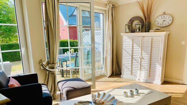 Un salon comprenant un canapé, une table basse et donnant sur une terrasse aménagée avec du mobilier d’extérieur.