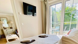 Une chambre avec un grand lit, un téléviseur fixé au mur, une fenêtre avec des rideaux et une vue sur l’extérieur.