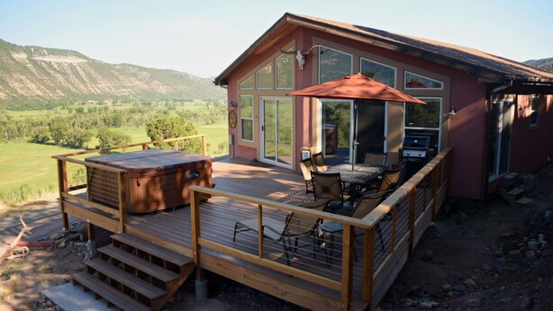 A wooden deck with a hot tub, outdoor seating, and a large glass door leading to a covered patio area. - Red Rock Overlook: A secluded mountain home high above the Uncompahgre River (Ridgway)