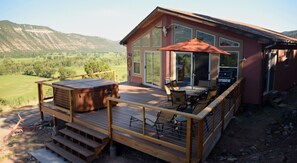 Une terrasse en bois dotée d’un jacuzzi, d’un espace salon extérieur et d’une grande porte vitrée donnant sur un patio abrité.