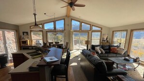 A spacious living area with a dining table, a sofa, and a coffee table. There are large windows providing a view of the outdoors. - Red Rock Overlook: A secluded mountain home high above the Uncompahgre River (Ridgway)