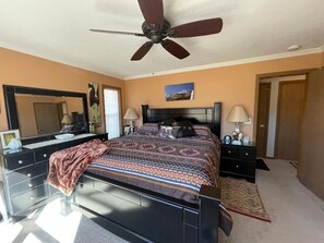 A bedroom with a bed, two bedside tables, a ceiling fan, a dresser, a mirror, and a door. - Red Rock Overlook: A secluded mountain home high above the Uncompahgre River (Ridgway)