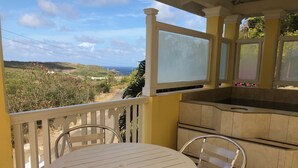 A balcony with a white table and chairs, a small kitchen area, and a view of the landscape. - South Sea House Luxurious Apt No 1 (Cap Estate)