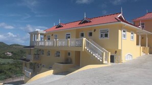 A multi-story yellow building with a red roof, a balcony, and a staircase leading to the upper floors. - South Sea House Luxurious Apt No 1 (Cap Estate)