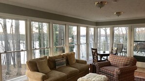 A cozy room with a large window, a sofa, a plaid armchair, and a dining table. - Spacious, Family-Friendly Lake House Retreat w/ a Private Large 2-Story Dock (Cumming)