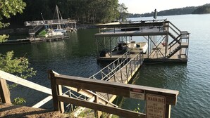 A dock with a warning sign, a boat, and a calm lake surrounded by trees. - Spacious, Family-Friendly Lake House Retreat w/ a Private Large 2-Story Dock (Cumming)