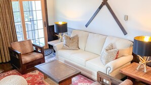 A cozy living room with a white sofa, wooden coffee table, and two armchairs. There are two lamps on side tables, a large window with curtains, and a patterned rug on the floor. - Whistlepunk #4 - Complete Renovation, Truly Slopeside, Near 2 Lifts & Village (Snowshoe)