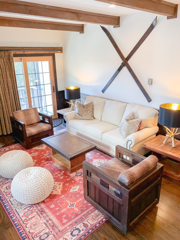 A cozy living room with a white sofa, wooden coffee table, and two armchairs. There are two lamps on side tables, a large window with curtains, and a patterned rug on the floor. - Whistlepunk #4 - Complete Renovation, Truly Slopeside, Near 2 Lifts & Village (Snowshoe)