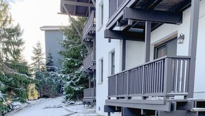 A snow-covered courtyard with a stone fire pit, wooden deck, and a building with balconies. - Whistlepunk #4 - Complete Renovation, Truly Slopeside, Near 2 Lifts & Village (Snowshoe)