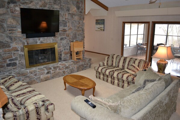 A living room with a stone fireplace, a flat-screen TV mounted above it, a patterned sofa, and a wooden coffee table.