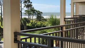 A balcony with a view of the ocean, surrounded by greenery and a clear sky. - Coastal King Couples Retreat Oceanfront Beach Property Convenient to Everything! (Hilton Head Island)