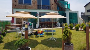 A brick building with a balcony, outdoor seating area with umbrellas, and a trampoline. - Jeju Sky Sea Pension (Jeju City)