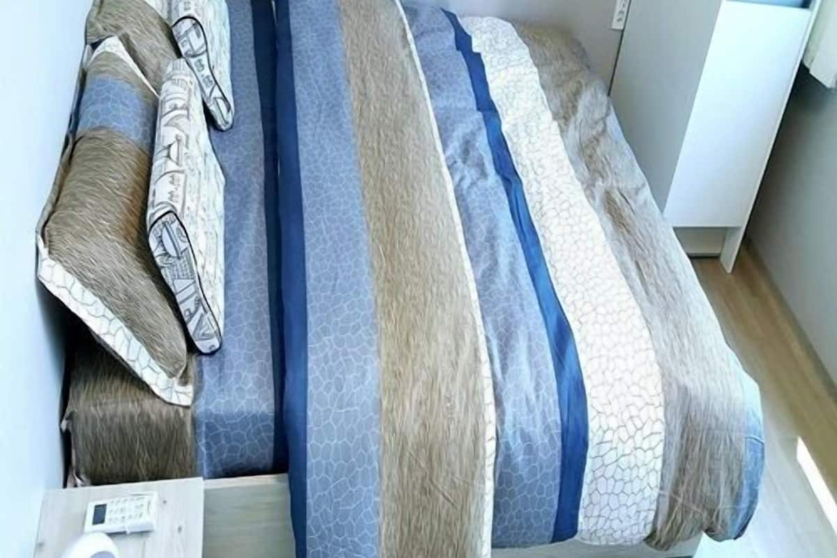 Una cama con colcha a rayas, almohadas y una mesita de noche con lámpara.