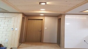 A hallway with a wooden ceiling, a door, and a white wall with a light switch. - Jeju Sky Sea Pension (Jeju City)