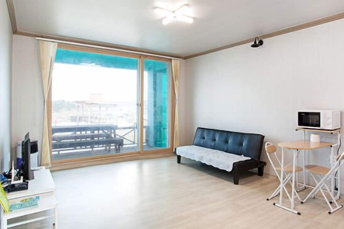 Una habitación moderna con sofá, una pequeña mesa con silla, microondas y vistas amplias a través de puertas correderas.