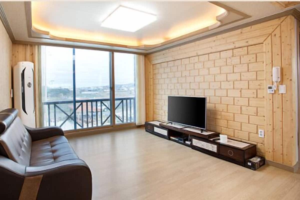 Una sala de estar moderna con un ventanal grande, un televisor de pantalla plana sobre un soporte de madera y un sofá de cuero.