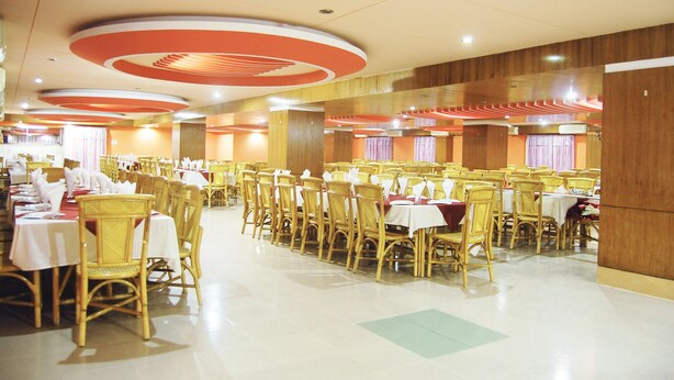 Un salón de banquetes con filas de mesas y sillas, paneles de madera en las paredes y diseños circulares en el techo.