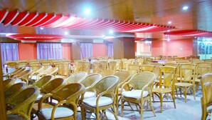 Un salón de conferencias con filas de sillas y mesas de mimbre, paneles de techo rojos y unidades de aire acondicionado.
