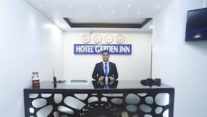 Un mostrador de recepción con un cartel que dice "HOTEL GARDEN INN" y relojes mostrando diferentes zonas horarias.