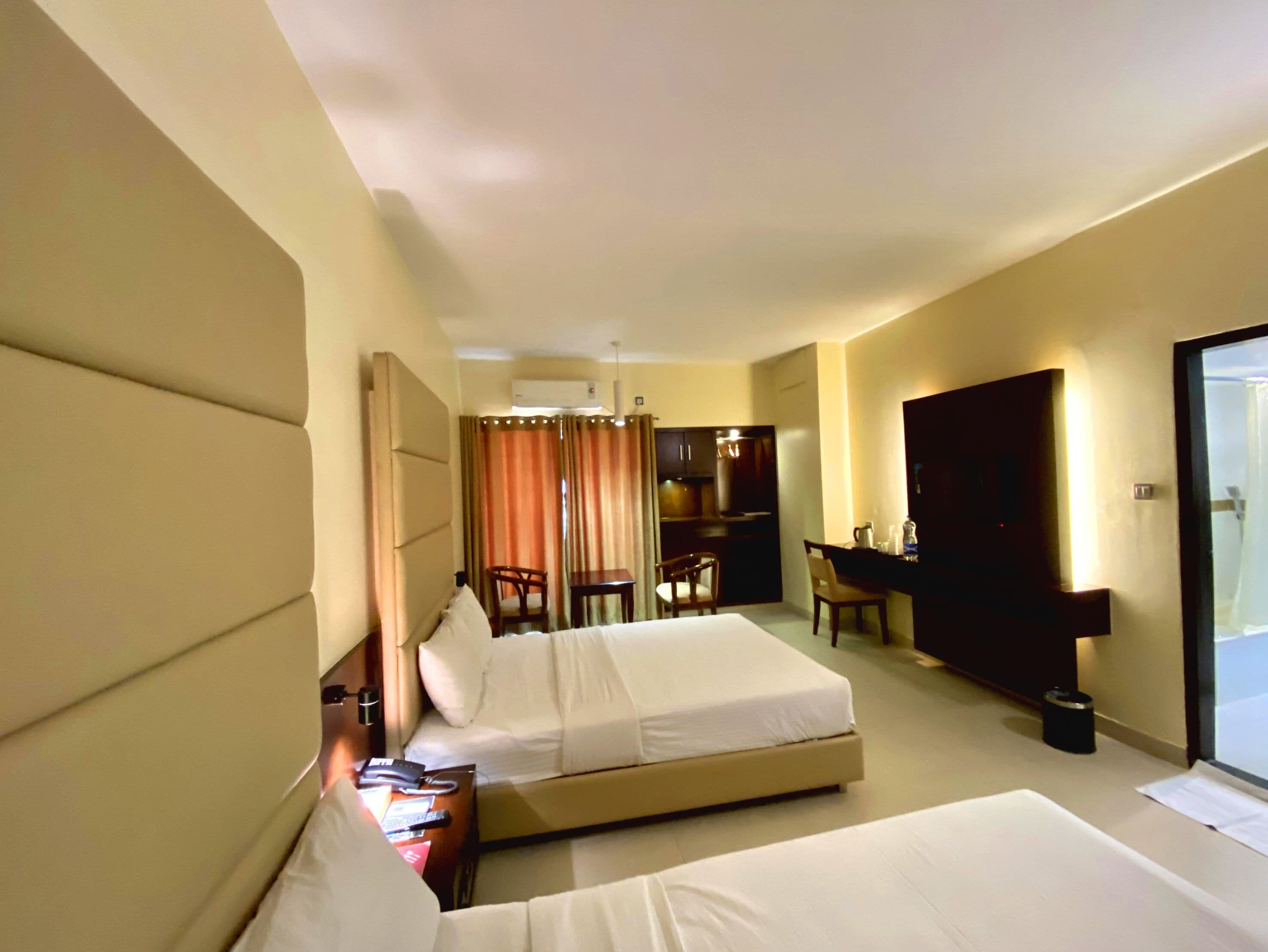 A hotel room with two beds, a desk, a chair, a minibar, and a bathroom.