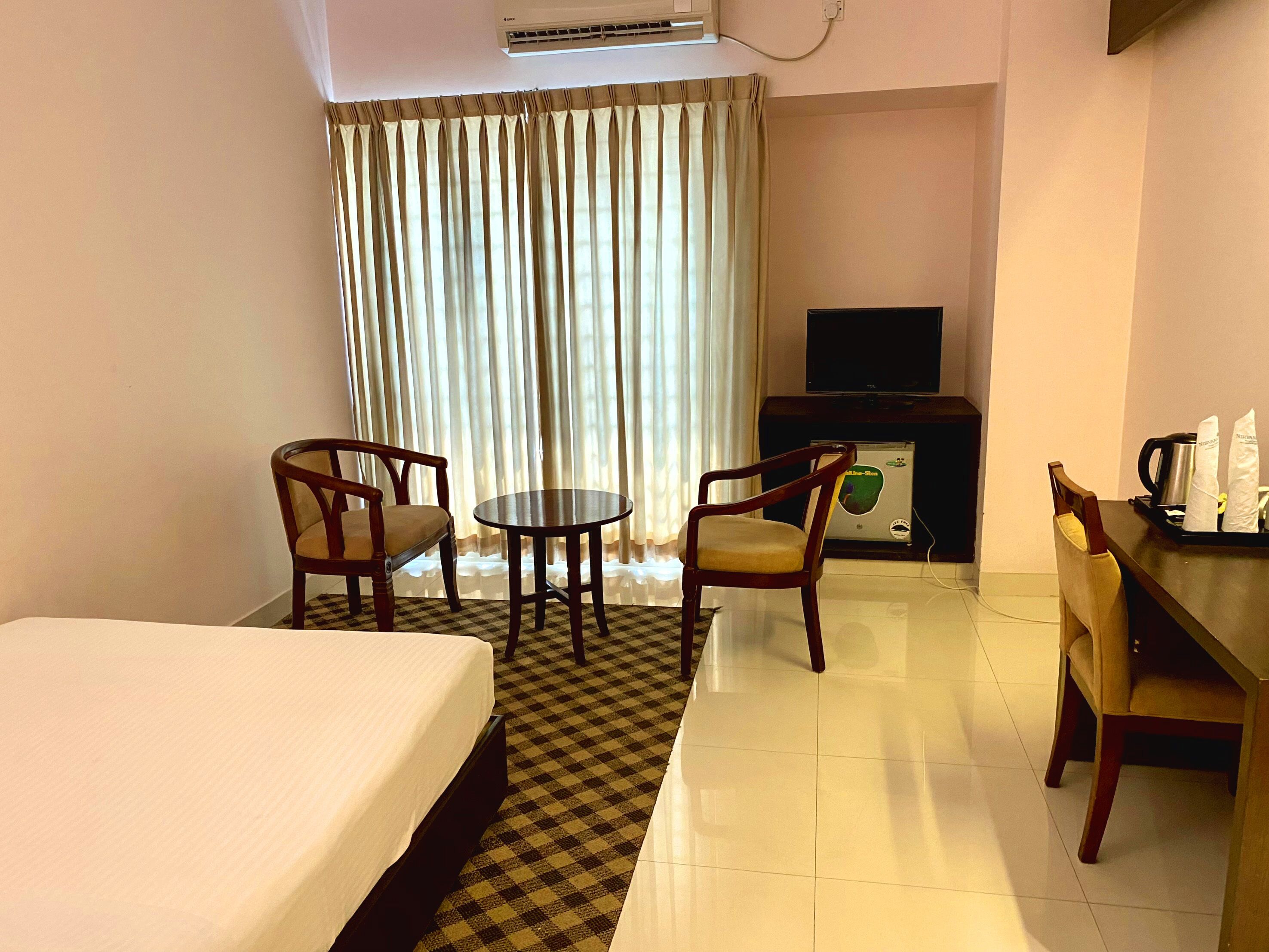 Una habitación de hotel con una cama, dos sillones, una mesita, un televisor y una cafetera.