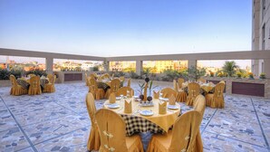An outdoor dining area with round tables set for a meal, surrounded by chairs with yellow covers. - Nirvana Inn (Sylhet)