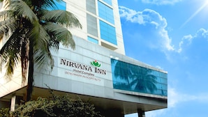 A modern hotel building with a sign reading "NIRVANA INN Hotel Complex BENCHMARK IN HOSPITALITY." - Nirvana Inn (Sylhet)