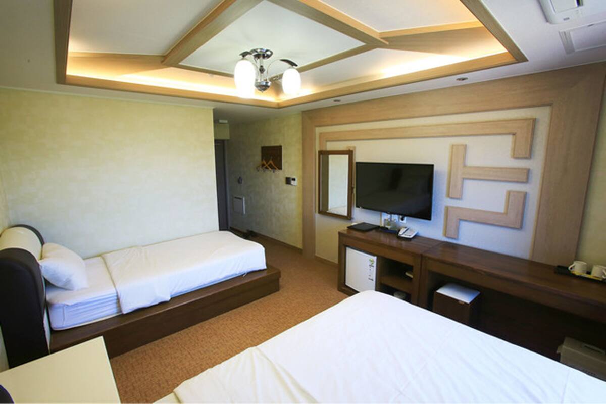 A hotel room with two beds, a desk, a television, and a mirror.