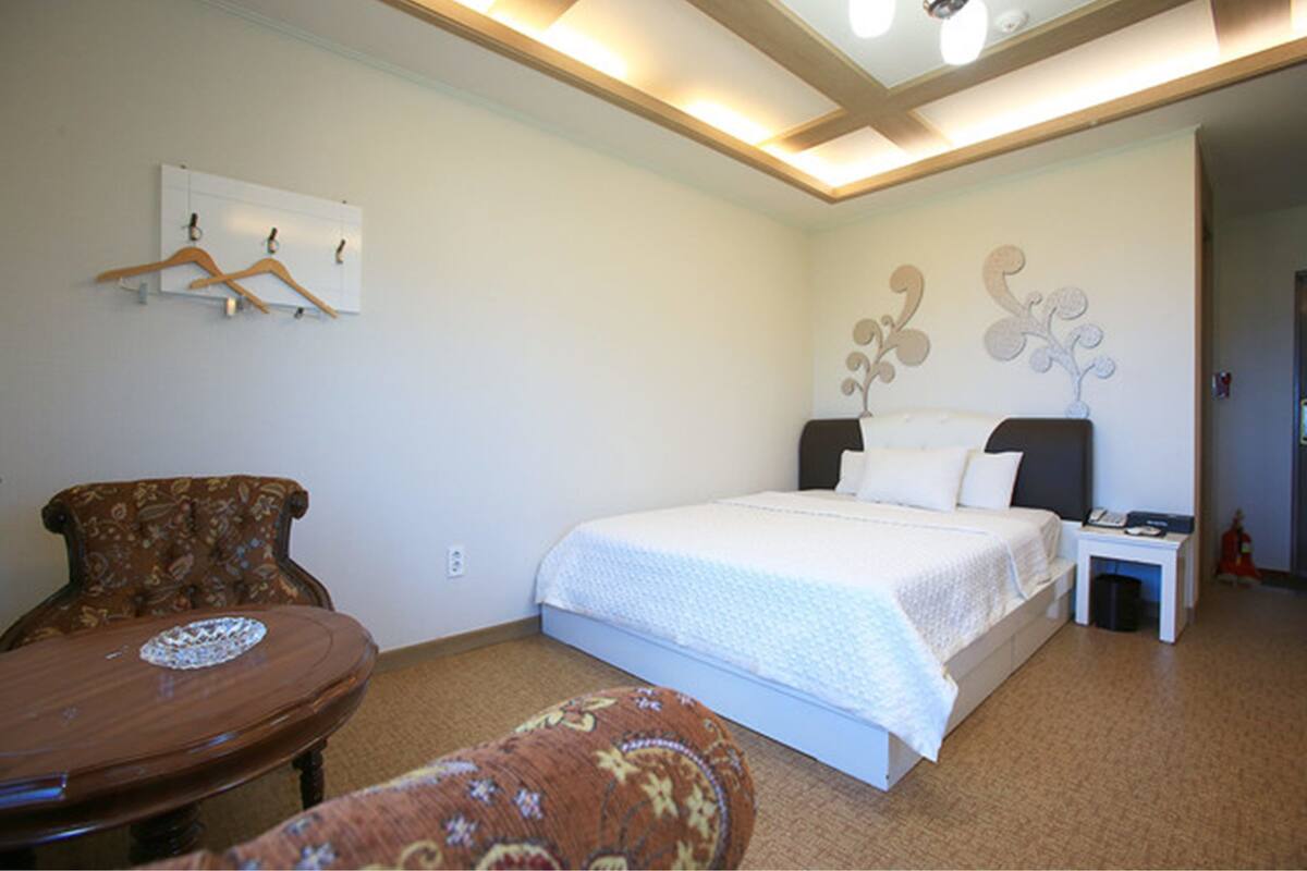 A bedroom with a bed, a chair, a small table, and a wall-mounted coat rack.