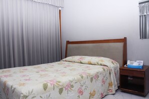 Una cama individual con una colcha estampada, un cabecero de madera y una mesita de noche con un teléfono y una caja.