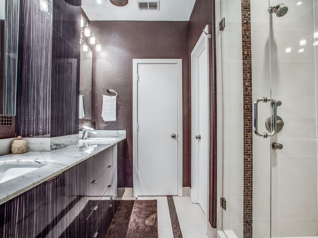 A modern bathroom with a large mirror, two sinks, a shower, and a door.