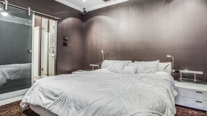 Ein modernes Schlafzimmer mit einem großen Bett, einer Duschkabine aus Glas und einem Nachttisch mit Lampe.