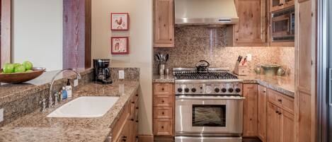A kitchen with granite countertops, stainless steel appliances, wooden cabinets, and a patterned rug.