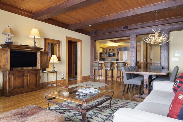 A spacious living room with a wooden ceiling, a television, a fireplace, and a dining area with a large table and chairs.