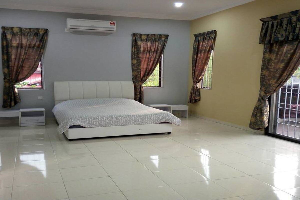 A bedroom with a large bed, two bedside tables, an air conditioning unit, and curtains on the windows.