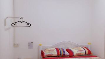 Quarto pequeno, com uma cama de solteiro, mesa de cabeceira de madeira, cabideiro e roupa de cama estampada.