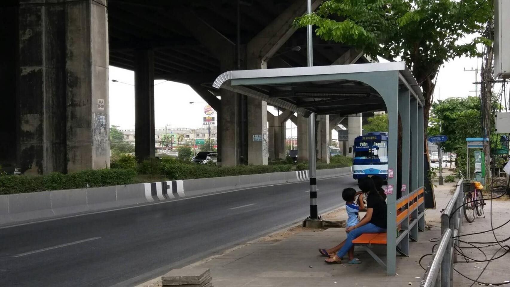 A bus stop shelter under a bridge with a road passing by.