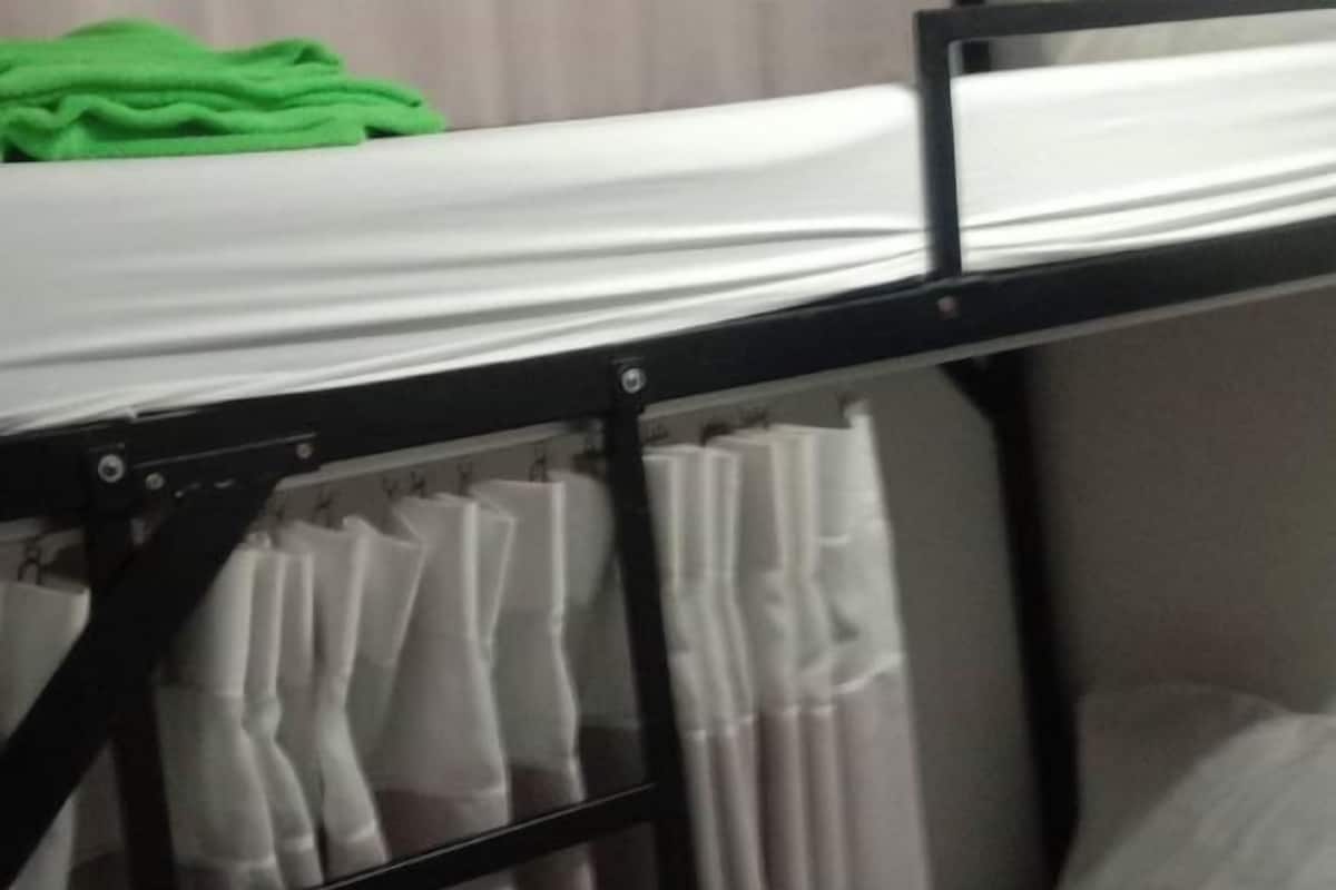 Ein Etagenbett mit einem grünen Handtuch auf der Oberliege und weißen Vorhängen an den Seiten.