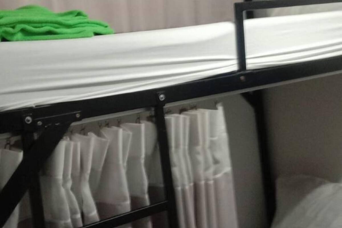Ein Etagenbett mit einem grünen Handtuch auf der Oberliege und weißen Vorhängen an den Seiten.