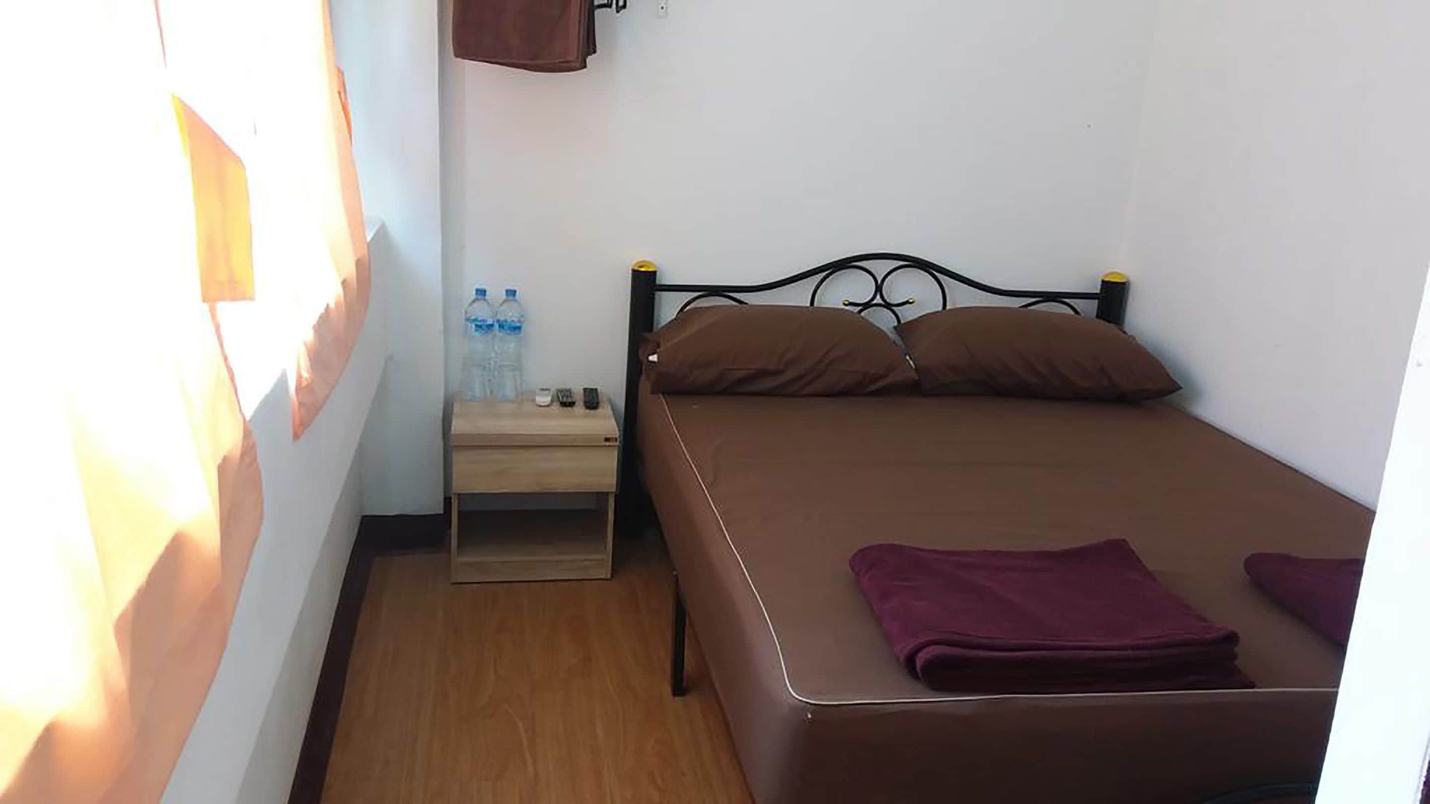 Un dormitorio pequeño y ordenado con una cama individual, una mesita de noche, suelo de madera y una estantería con objetos personales.