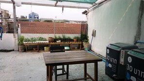 A rooftop patio with a wooden table, potted plants, and two water dispensers.