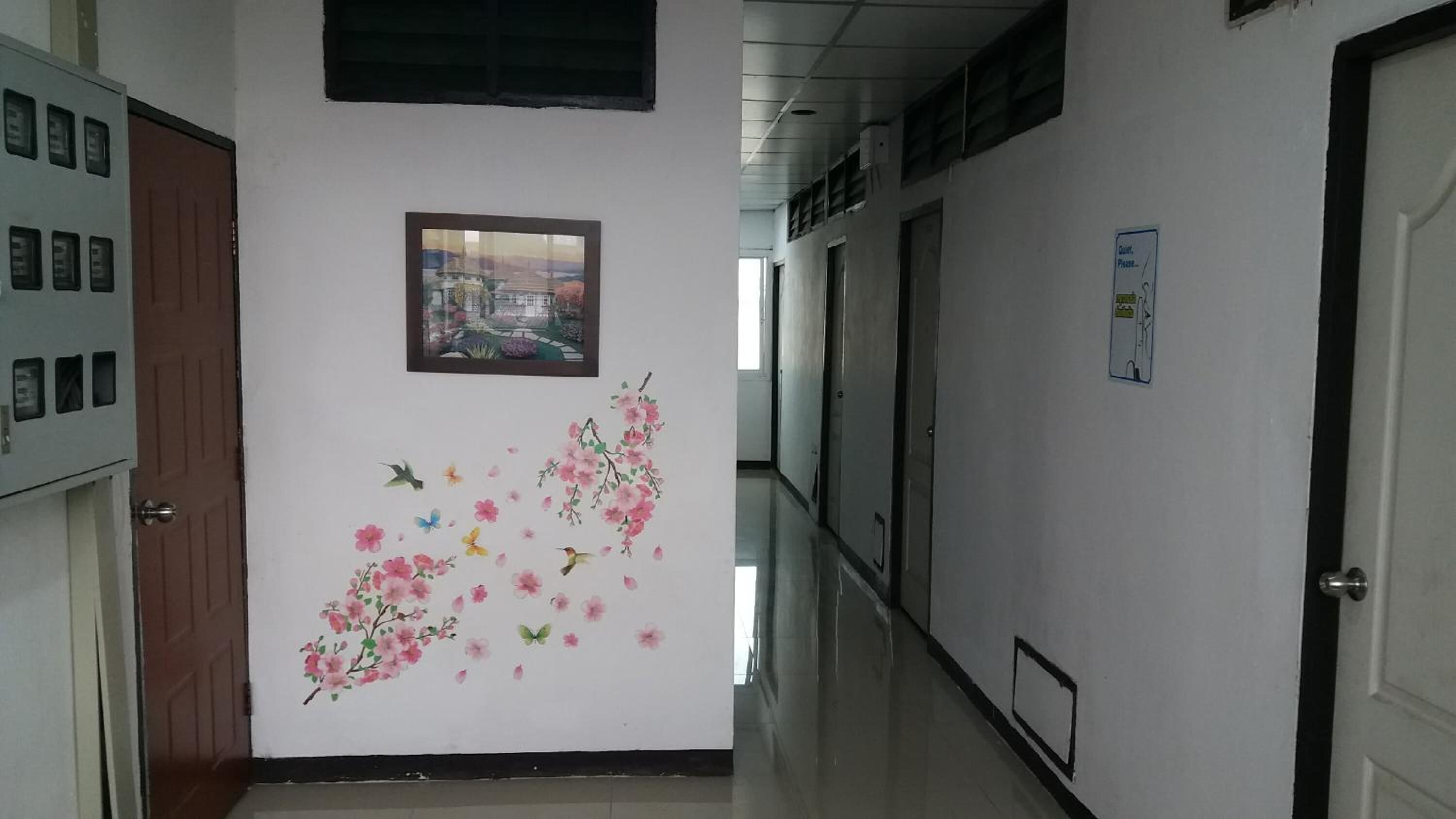 Un pasillo con un mural floral, un cuadro enmarcado y una puerta con un cartel.