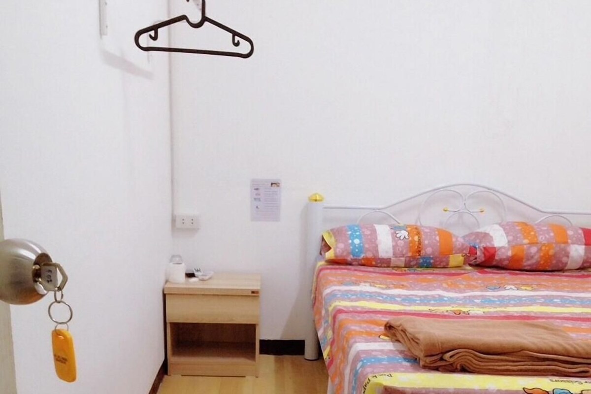 Una habitación pequeña y limpia con cama, mesita de noche y perchero.