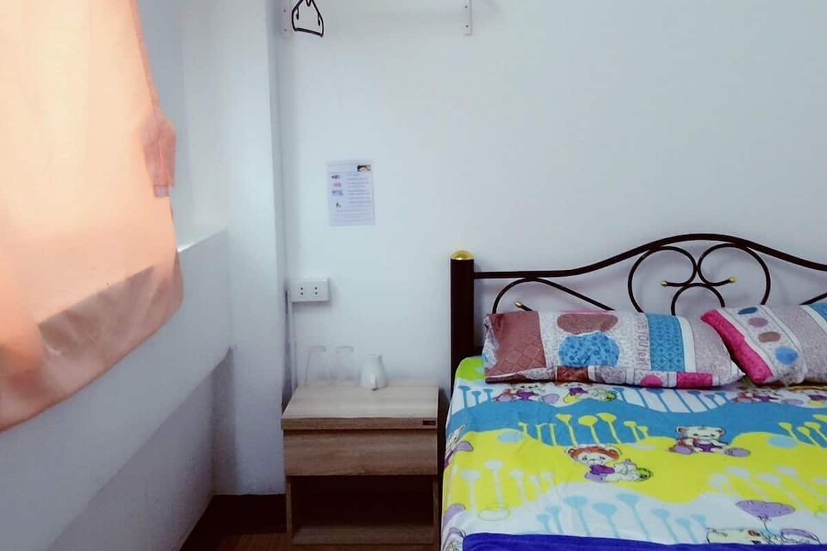 A small, clean room with a bed, a bedside table, and a wall-mounted air conditioner.