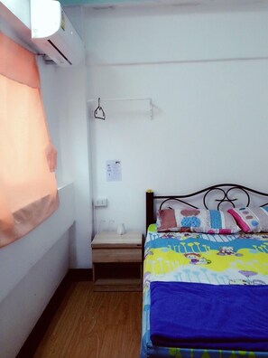 A small, clean room with a bed, a bedside table, and a wall-mounted air conditioner.