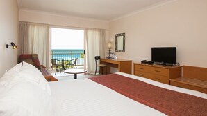 Une chambre d’hôtel équipée d’un lit, d’un bureau, d’une chaise, d’une télévision et d’un balcon avec vue sur la mer.