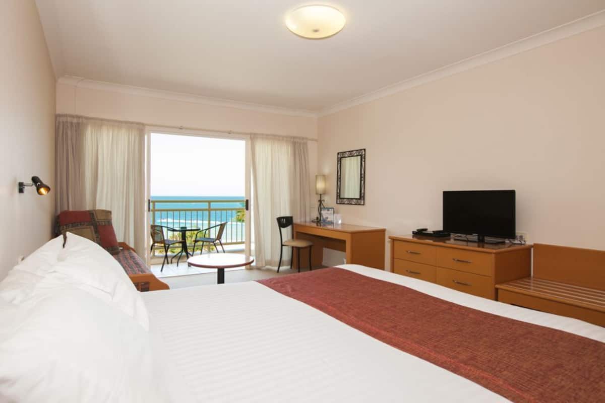 A hotel room with a bed, desk, TV, and a balcony with a view.