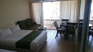 Une chambre d’hôtel avec un lit, un canapé vert, une petite table et un balcon avec des chaises.